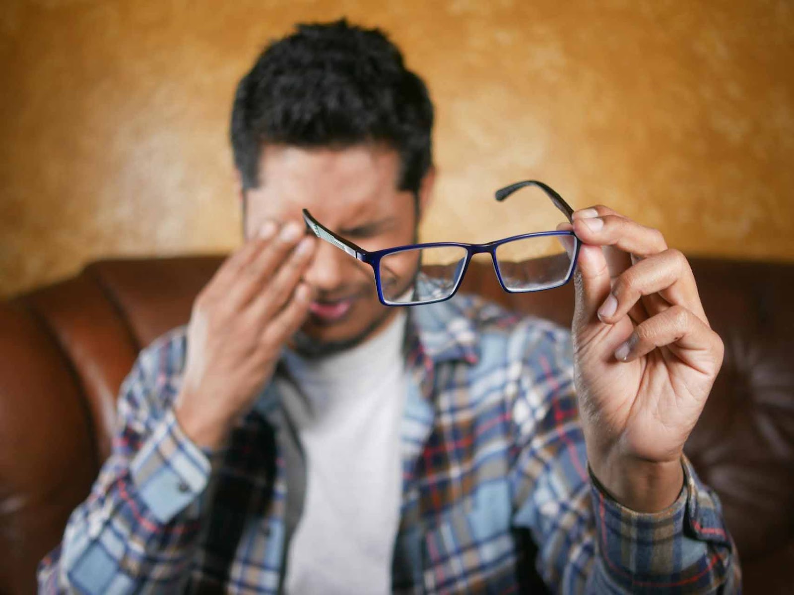 A man with blurry vision is holding glasses and massaging his eyes.