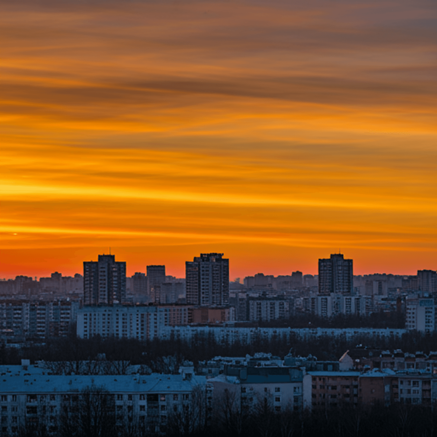 A serene sunset casting warm orange hues over a cityscape with high-rise buildings.