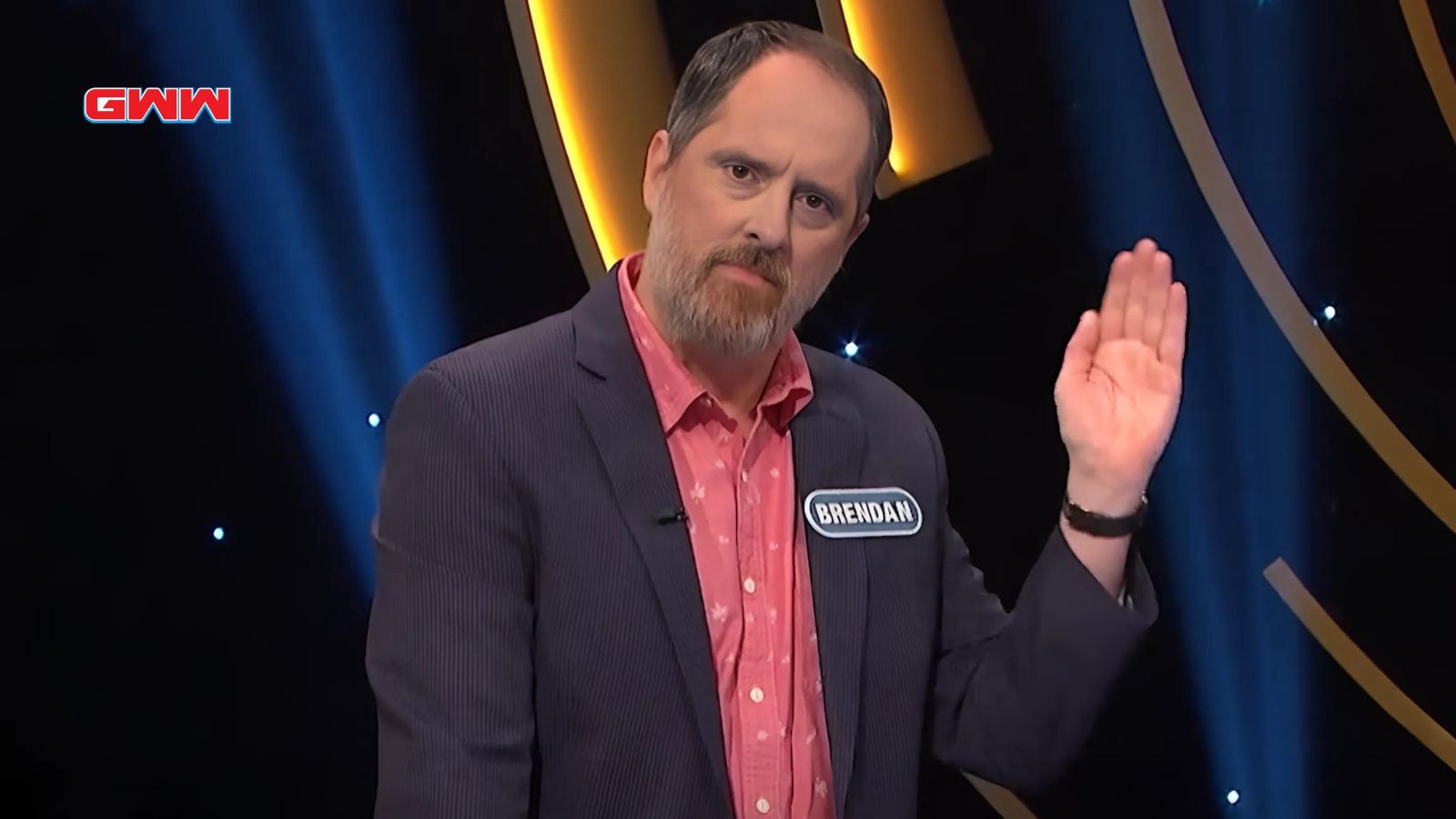 Contestant Brendan waving on a game show stage, wearing a blazer.