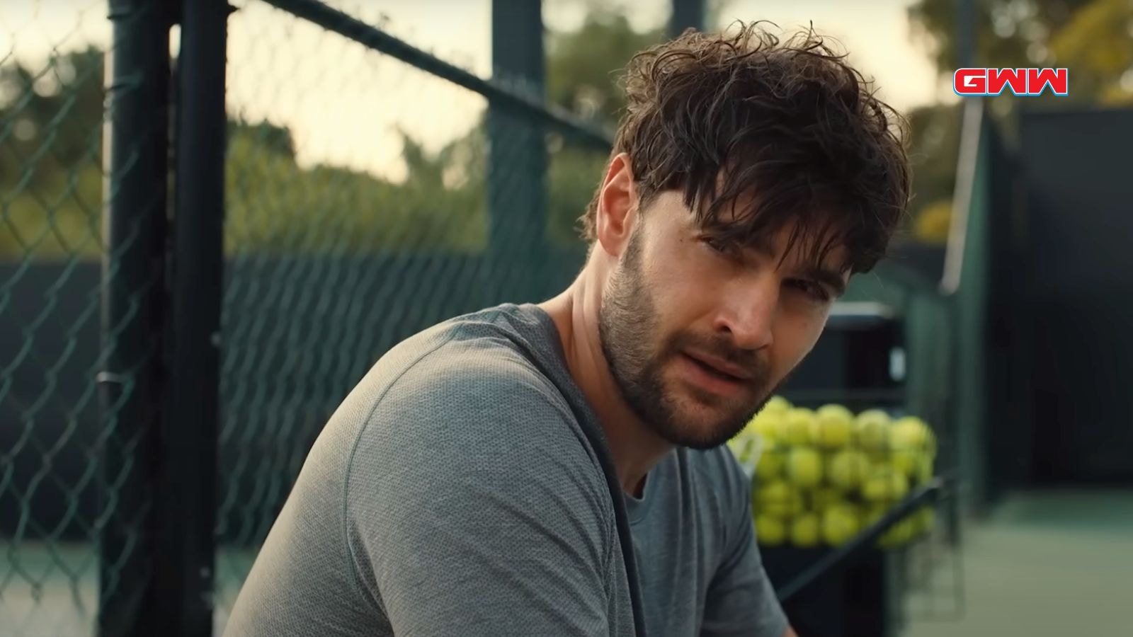 Matt sitting by the tennis court, appearing thoughtful.