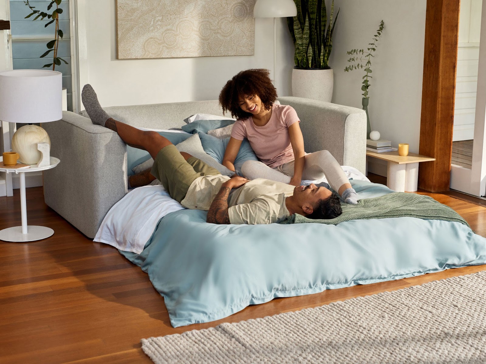 A young couple relax on their converted sofa bed in a corner of a compact living room