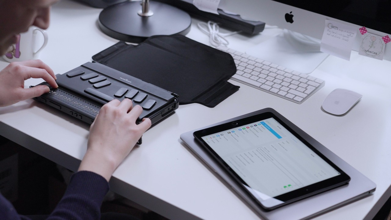 A person typing on a Braille for computer keyboard while using a tablet and desktop setup