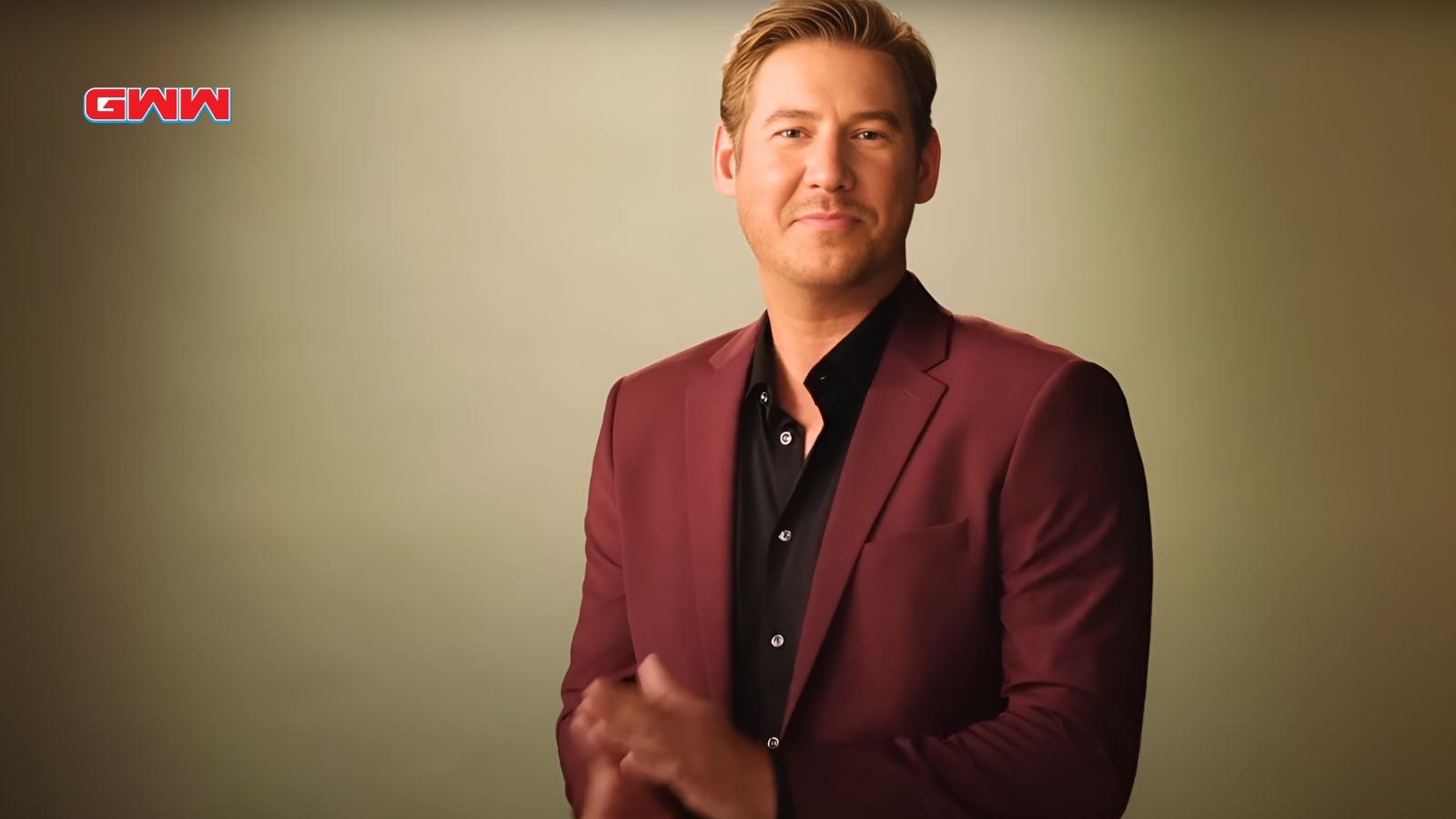 Austen Kroll in a burgundy suit smiling confidently at the camera.