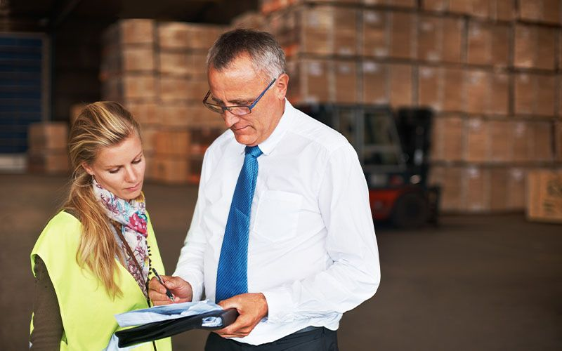 A man and woman in a warehouse analyze a clipboard, engaged in discussions about IC-DISC and transfer pricing.