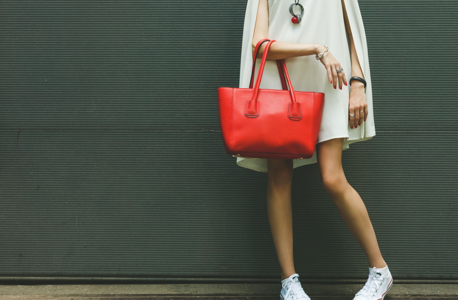 A cropped photo of a well-dressed woman wearing slim, trendy sneakers and carrying a large red handbag.
