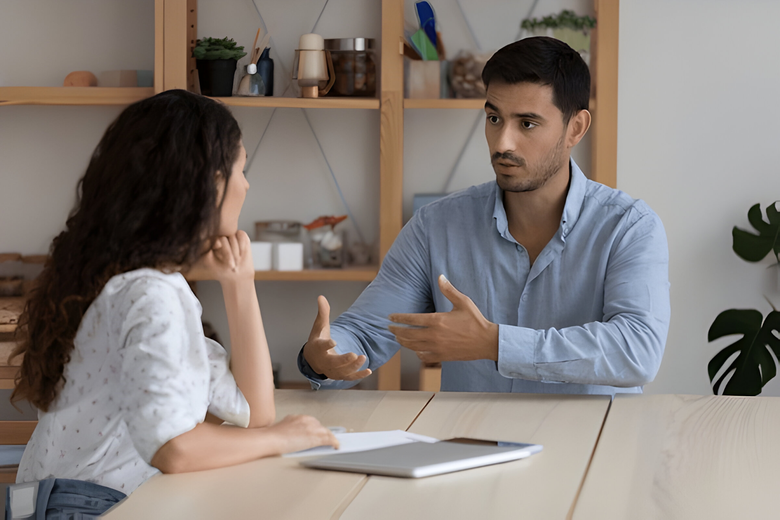 Two individuals engaged in a focused conversation across a table, with one person gesturing as they speak, symbolizing the assessment of communication skills.