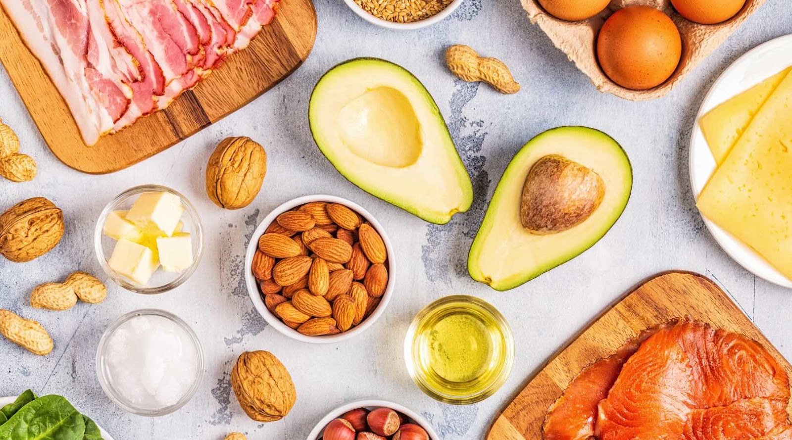 Assortment of keto-friendly foods including bacon, avocado, nuts, eggs, cheese, salmon, and healthy oils, highlighting ingredients rich in healthy fats and low in carbohydrates.