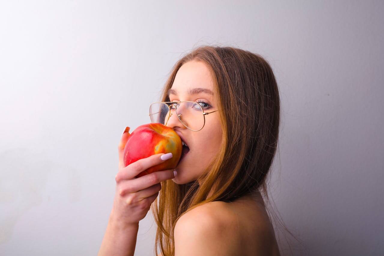 A woman with glasses enjoys an apple, highlighting the connection between diet and healthy hair and scalp.