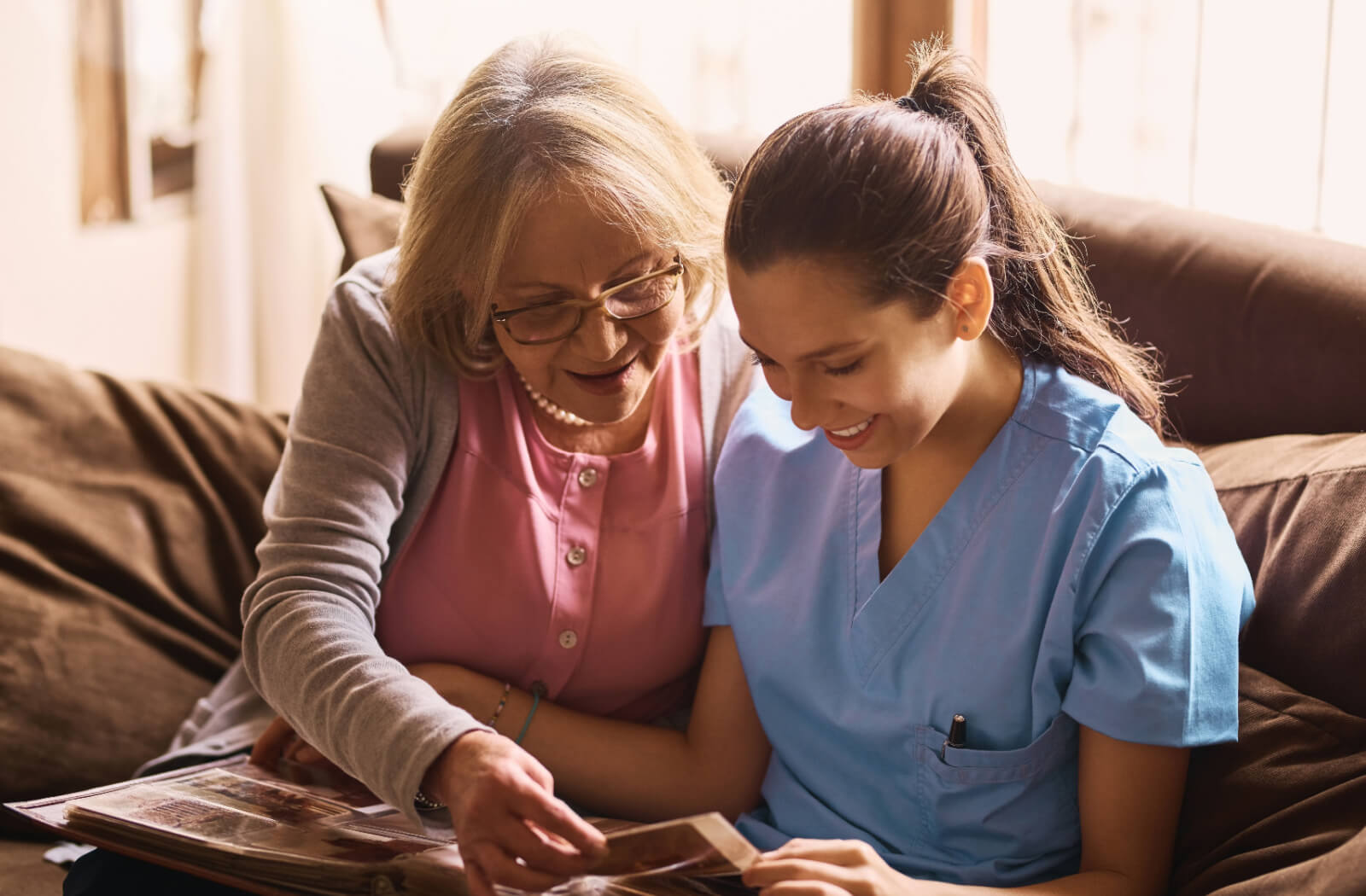 An older adult and a caregiver smiling while looking through a photo album together in memory care.