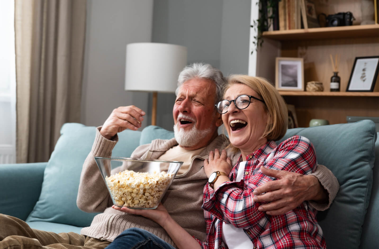 An older married couple laughing while eating popcorn and watching a movie about Alzheimer's disease.