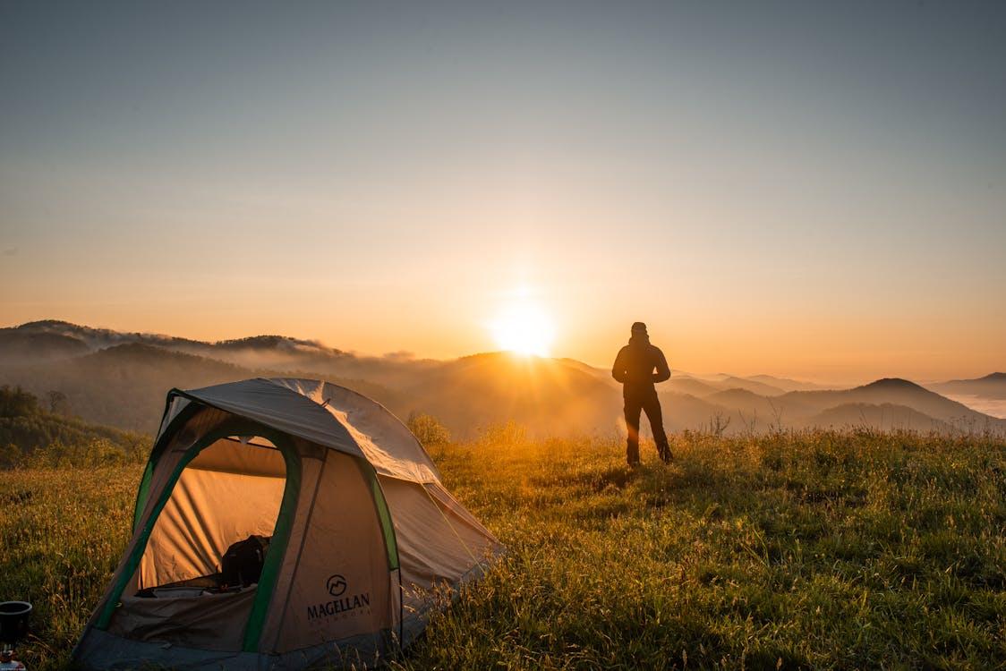 Free A camper enjoys the sunrise in a mountain setting with a tent. Perfect nature escape. Stock Photo