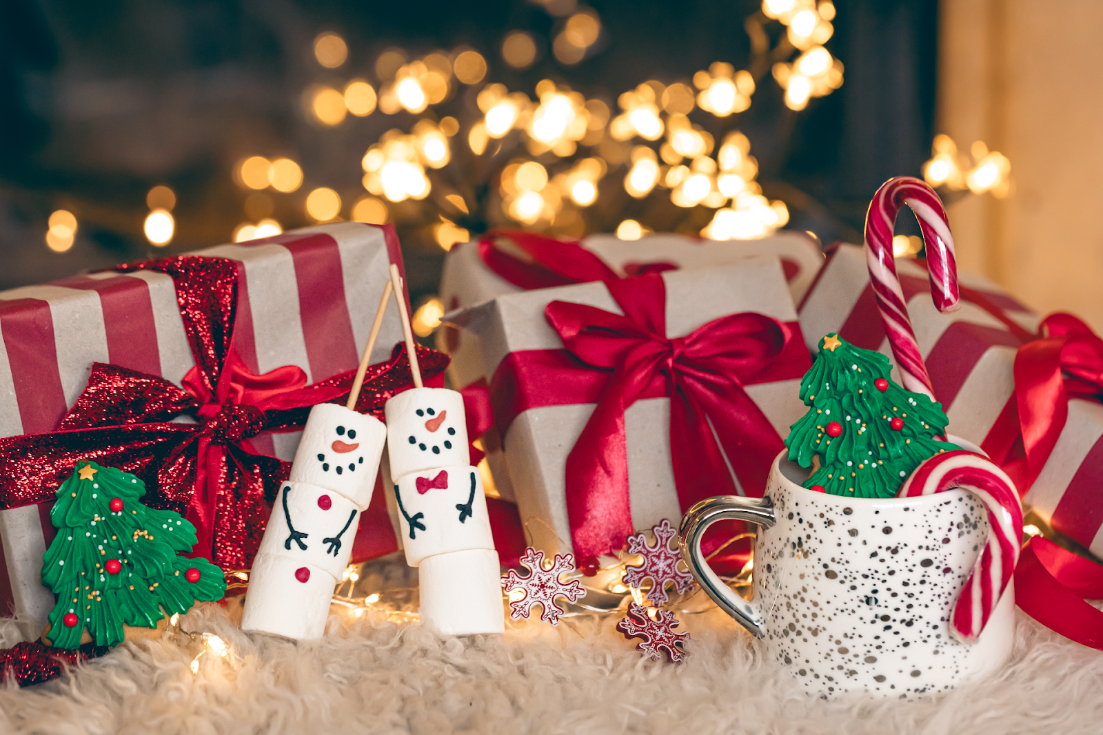 Christmas gifts covered in red ribbons amidst a backdrop of fairy lights