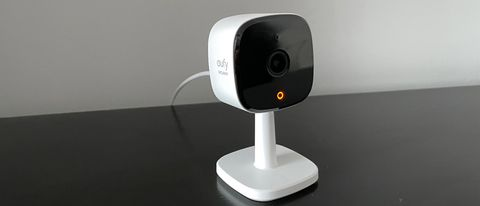 How to Reset Eufy Indoor Camera: A white Eufy indoor security camera on a stand, placed on a black surface with its lens facing forward and an orange indicator light glowing."