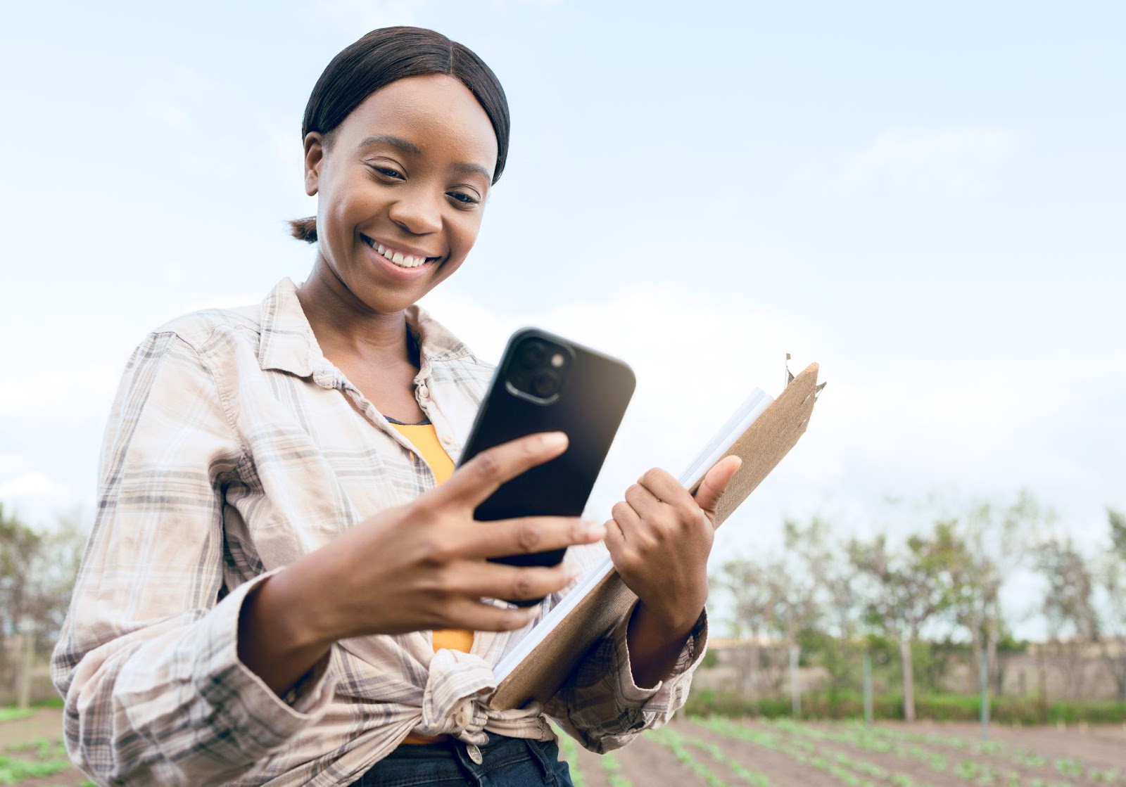 A woman inputs ecology research data into her mobile phone while holding a clipboard, demonstrating the efficiency of digital data collection in fieldwork.