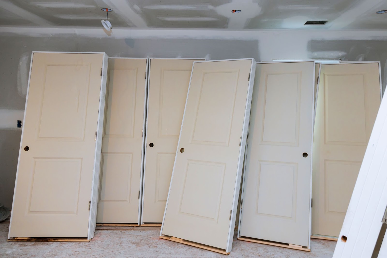 A few white replacement doors are leaning against a wall in a partially renovated space, ready to be installed as part of a home improvement project.