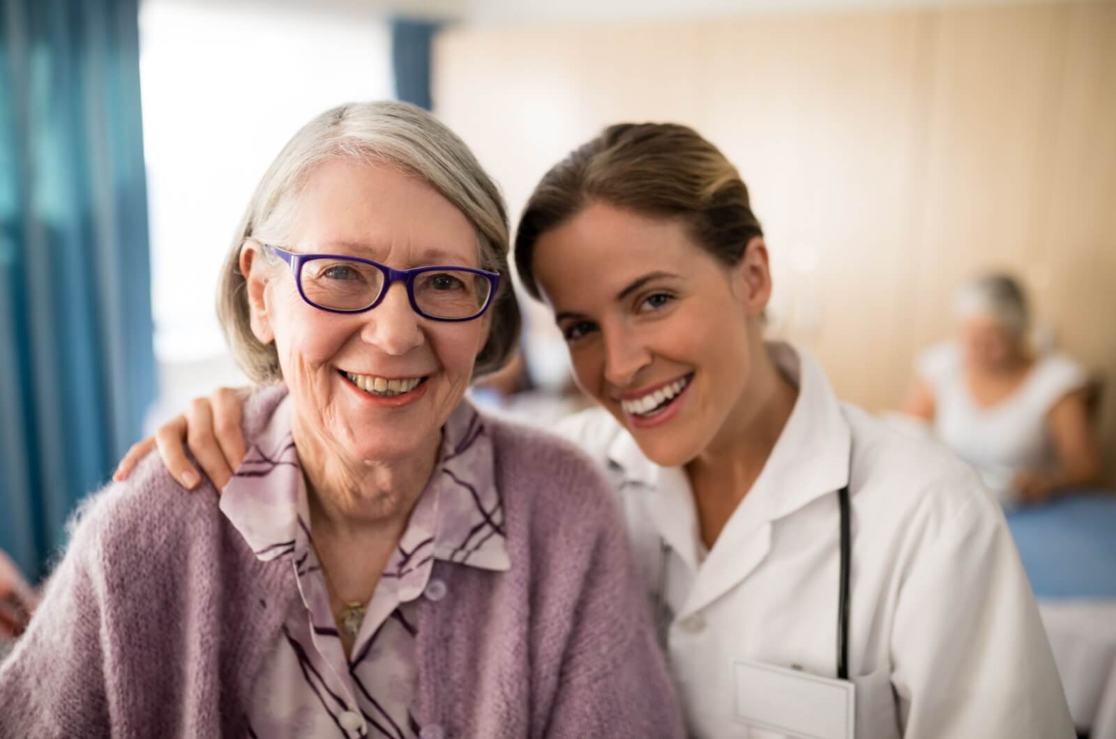 A smiling healthcare professional with their arm around an older adult's shoulder in a personal care community.