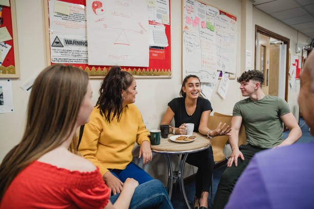 Teenagers Relaxing with Tea at Youth Club Small group of teenagers are enjoying tea and biscuits at youth club. They are all talking with the youth club leader. school club stock pictures, royalty-free photos & images