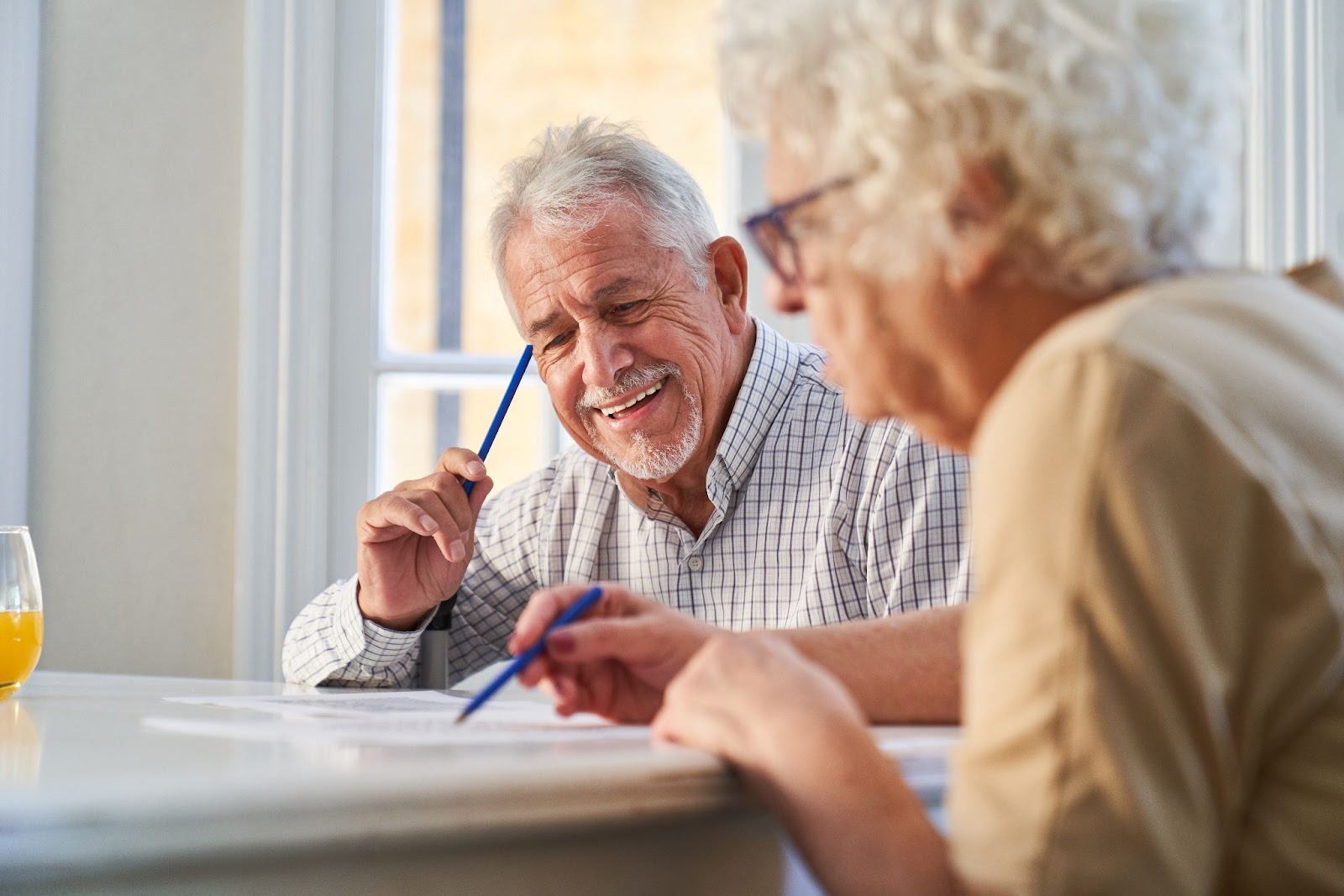 A pair of seniors in memory care smiling while solving a word puzzle.