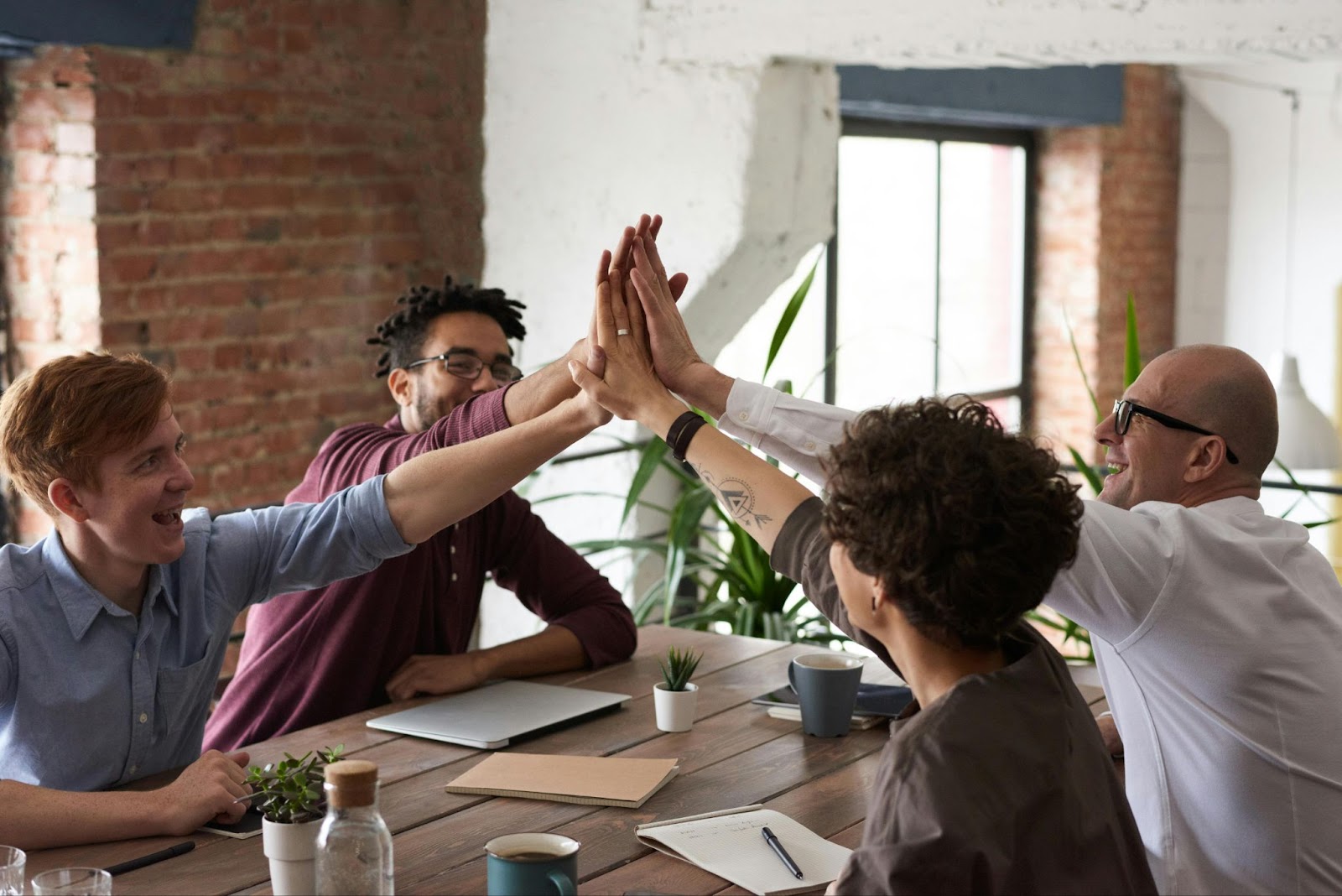 4 men sitting at a table giving each other a high five.
