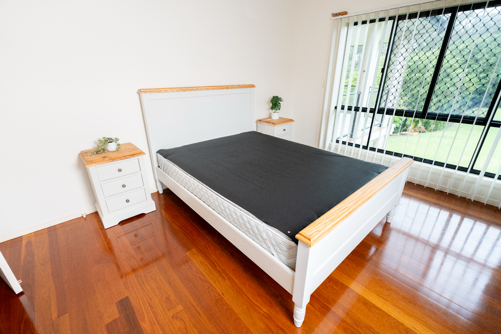 Minimalist bedroom featuring a grounding mattress cover on a queen-sized bed, with white wooden frame and natural wood accents, promoting better sleep and wellness.