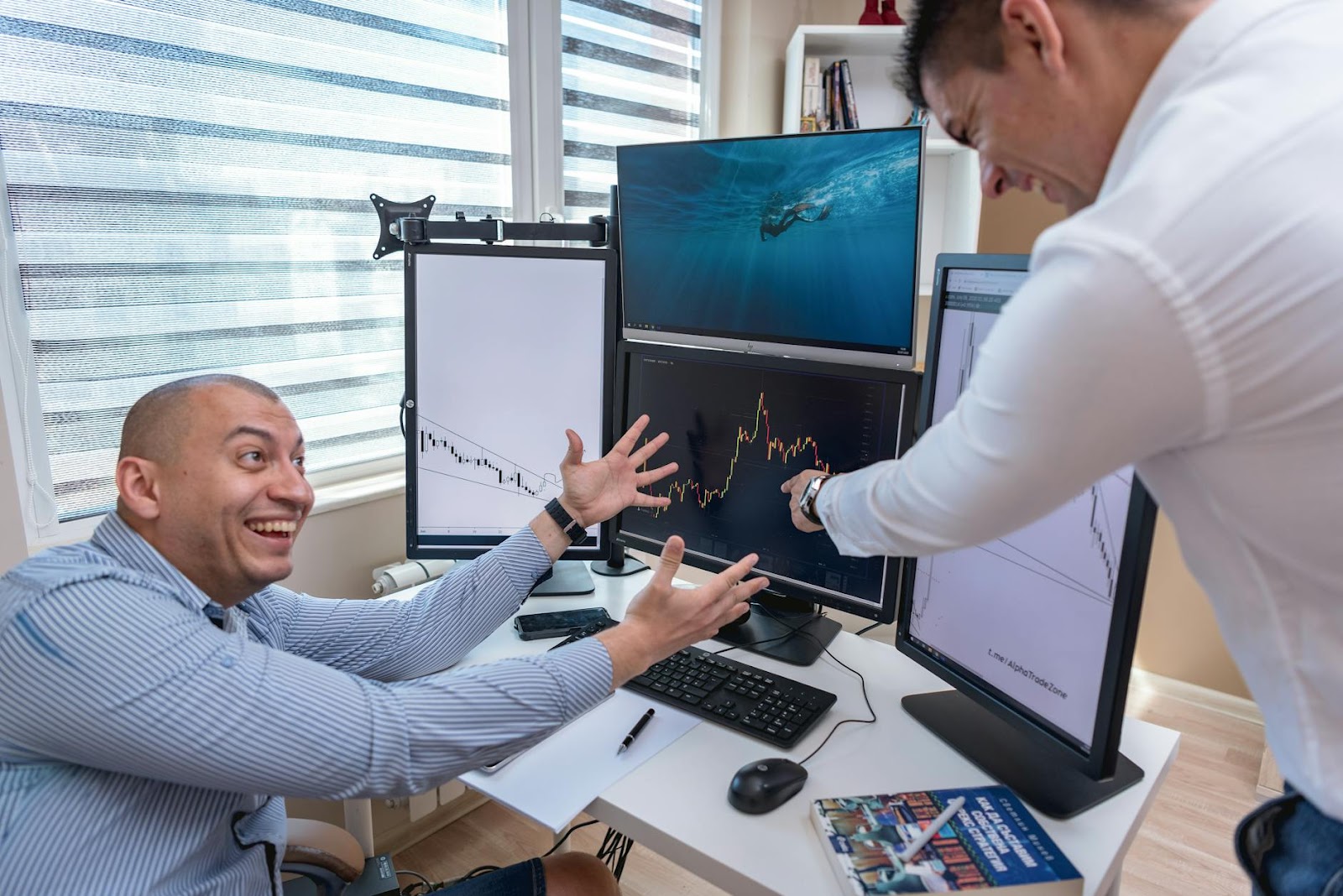 Two businessmen enthusiastically analyzing market charts on computer monitors in a modern office.