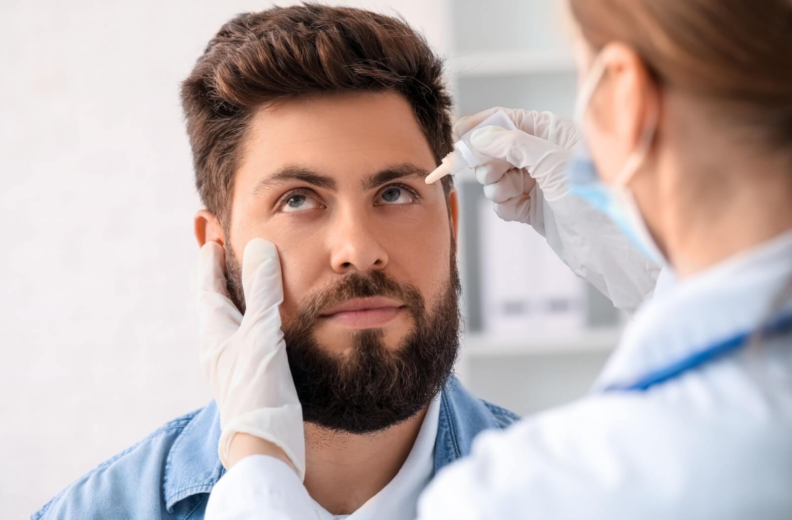 An eye doctor administering medical eye drops to a patient.