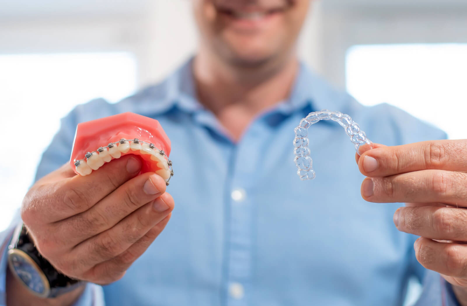 A close-up image of a dentist holding an Invisalign arch and a model of teeth with braces.