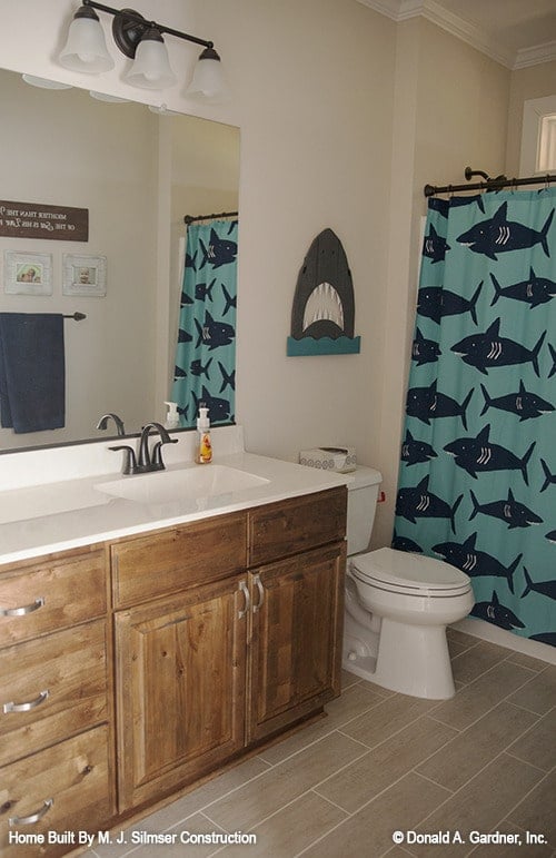 This bathroom has a wooden vanity, a toilet, and a shower area enclosed in a shark patterned curtain.