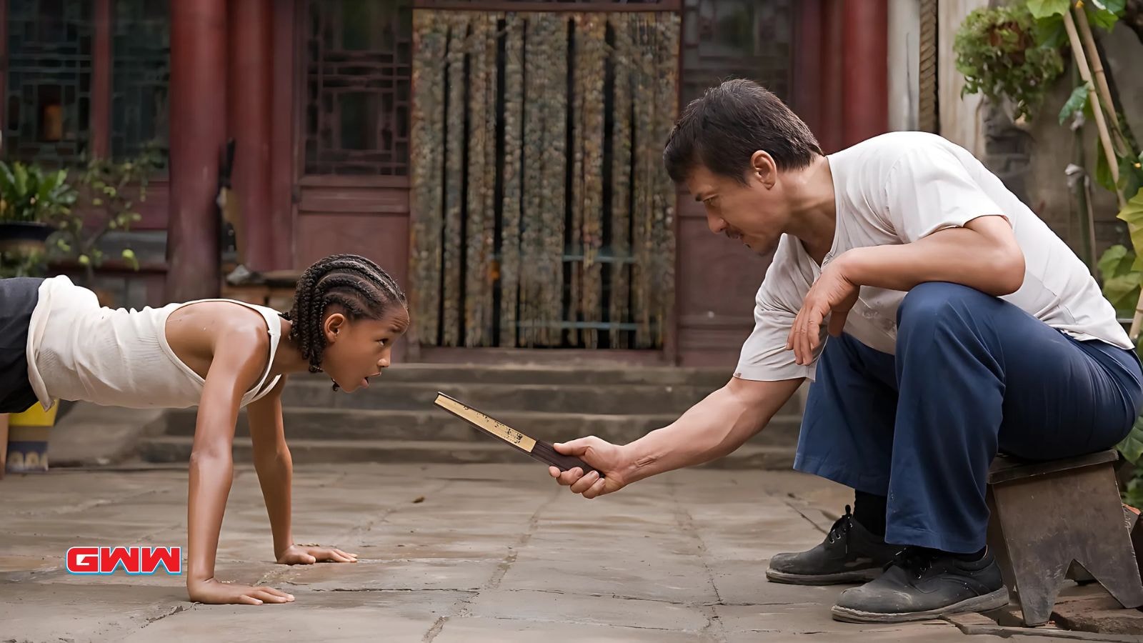 Jackie Chan supervising Jaden Smith doing push-ups during martial arts training.