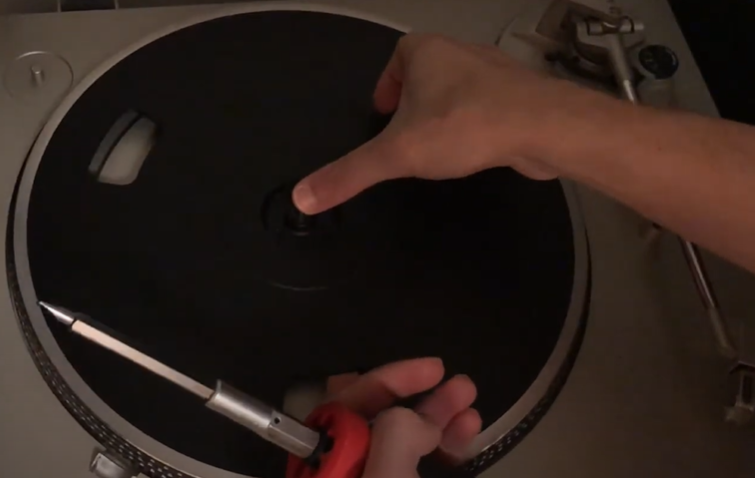 A person using a screwdriver to work on a turntable's platter.