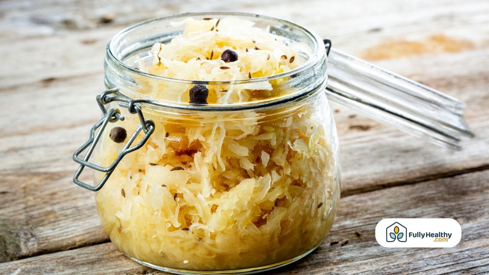 A jar of Sauerkraut with spices on rustic wooden surface.