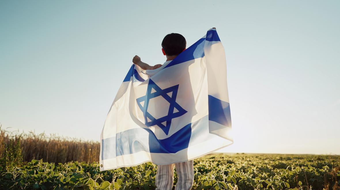 child faces away from the camera holding Israel's flag around him