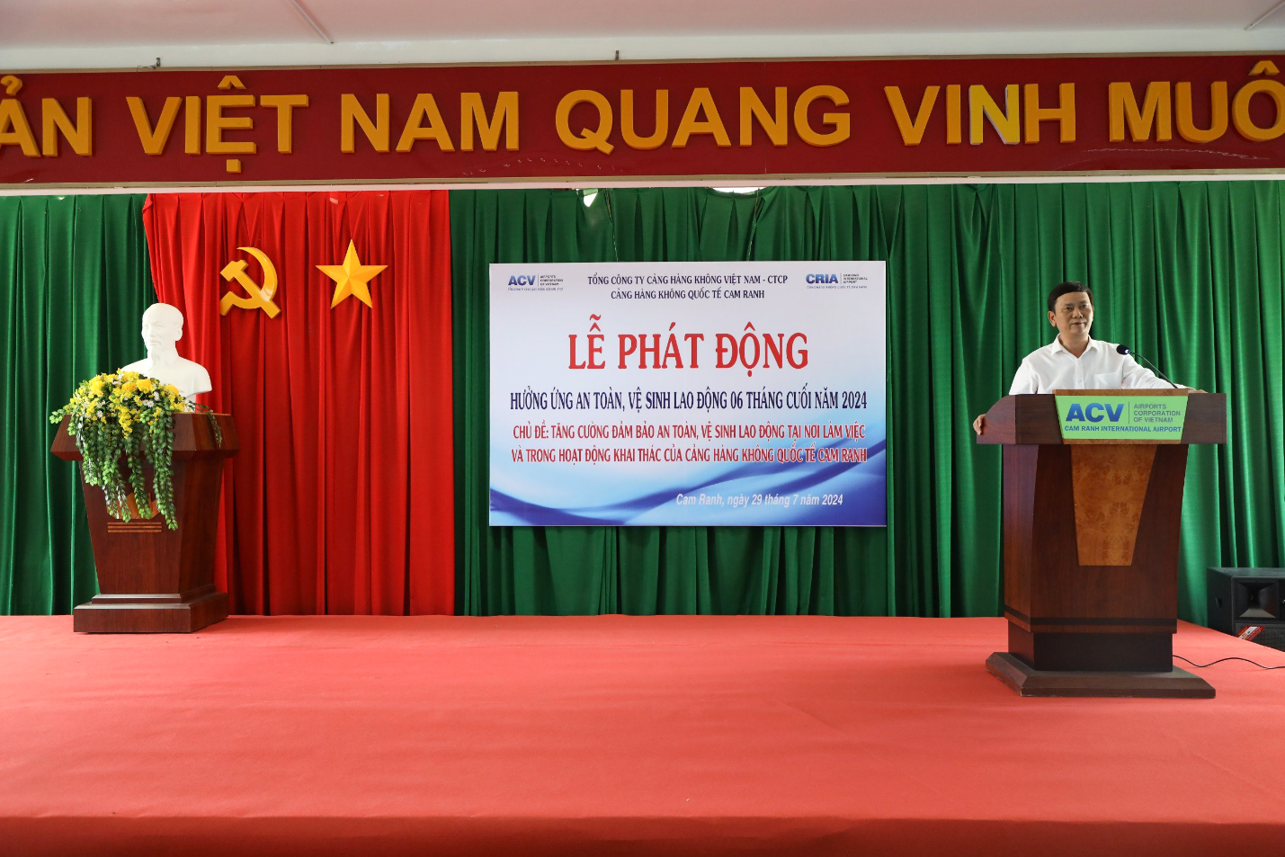 A person standing at podiums with a sign on the wallDescription automatically generated