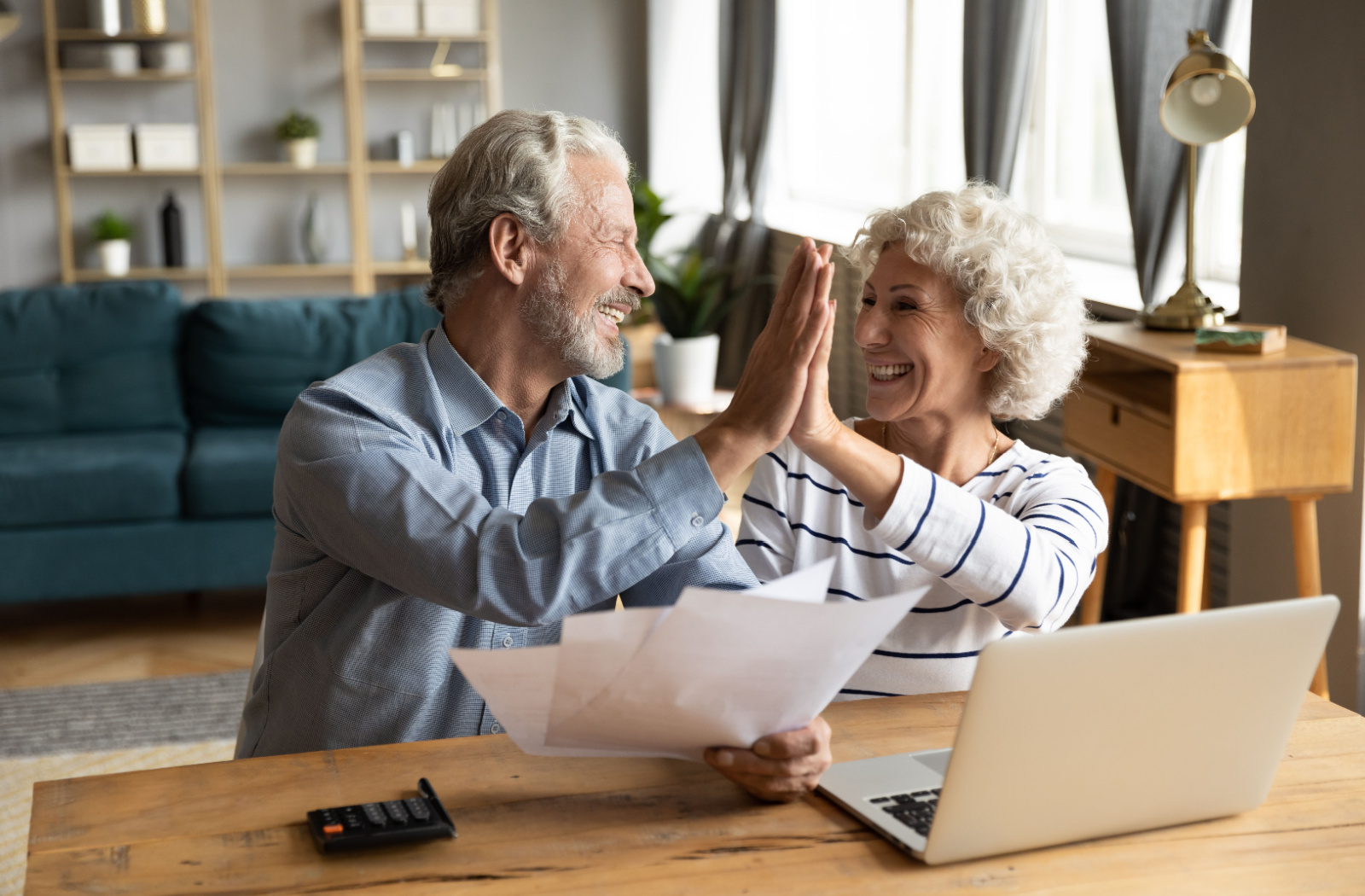 An older couple high-fiving in their living room while comparing their trivia answers in front of their laptop.