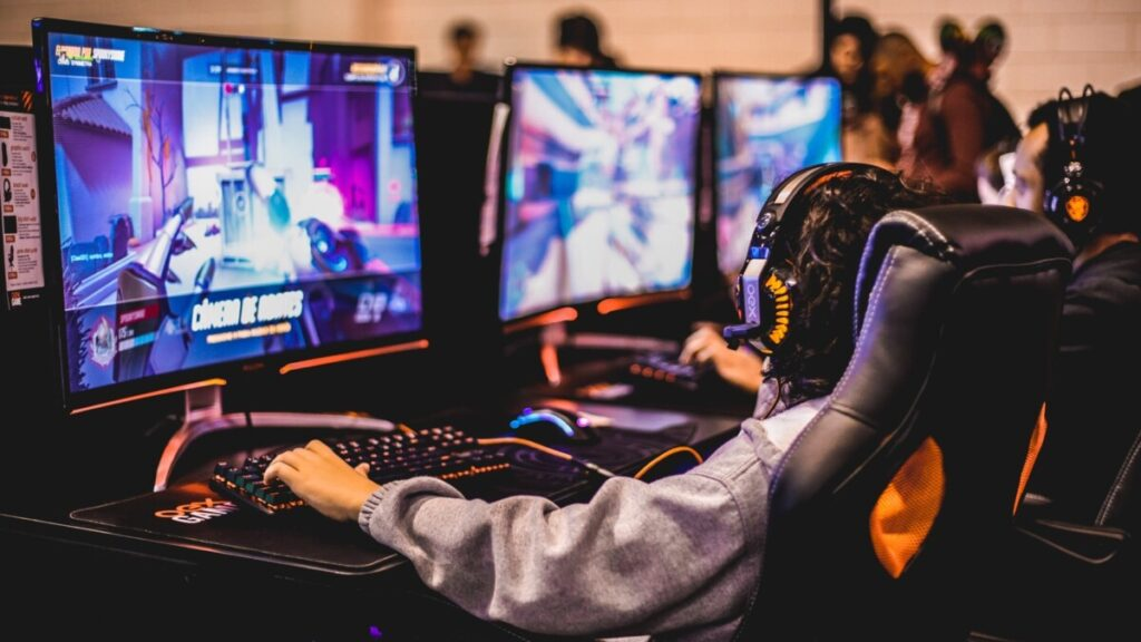 Jogadores de e-sports aparecem encostados em cadeira gamer, com a interface de Valorant aberta em seus computadores.