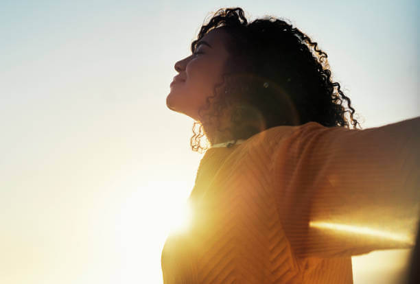 A woman smiling with her eyes closed, basking in the warm sunlight—radiating calmness and balance, a sign of healthy, low cortisol levels.