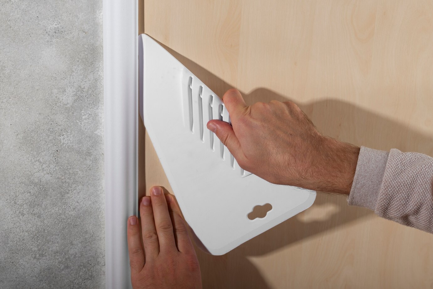 A person using a white plastic smoothing tool to press and align material along a Garage Doors near a corner with a white molding, ensuring a clean and precise finish