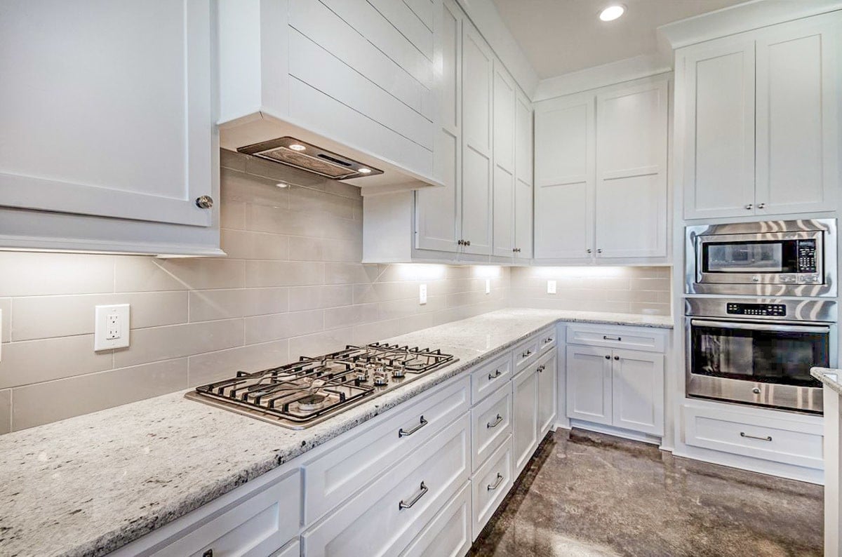 A closer look at the white cabinetry, double wall oven, and a built-in cooktop fitted on the granite countertop.