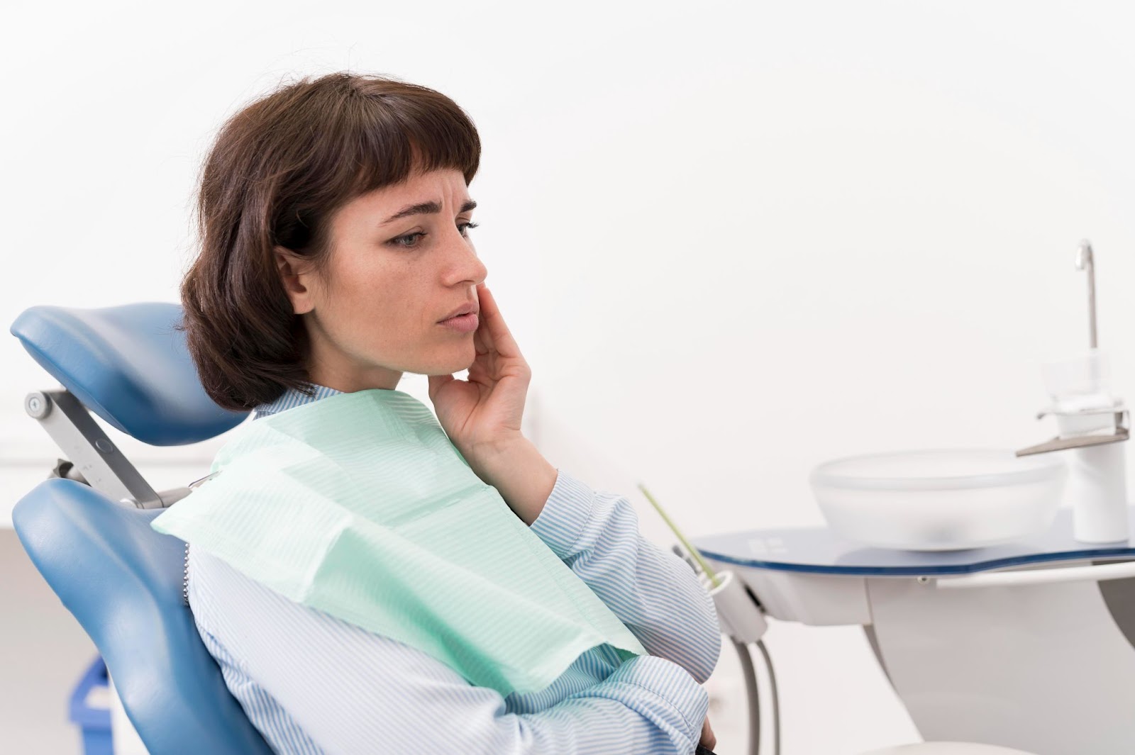 Woman sitting in a dental chair, touching her cheek in discomfort due to tooth sensitivity.