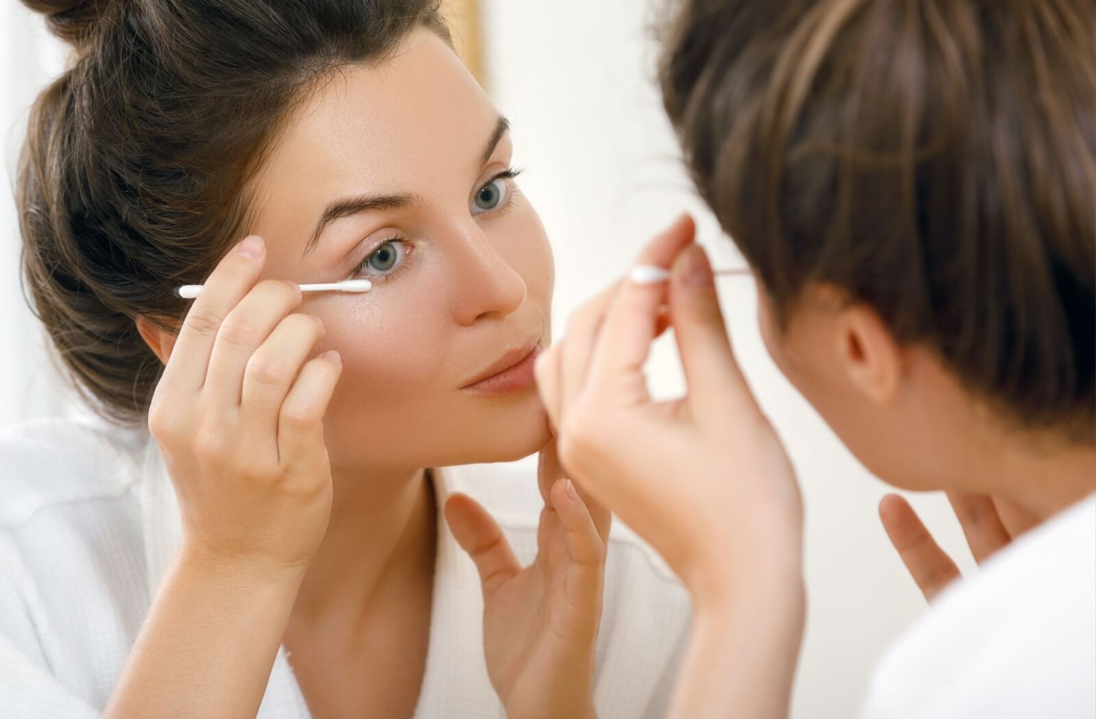 A young adult cleans their eyelids using a Q-tip as part of their nighttime routine to prevent eye issues like styes