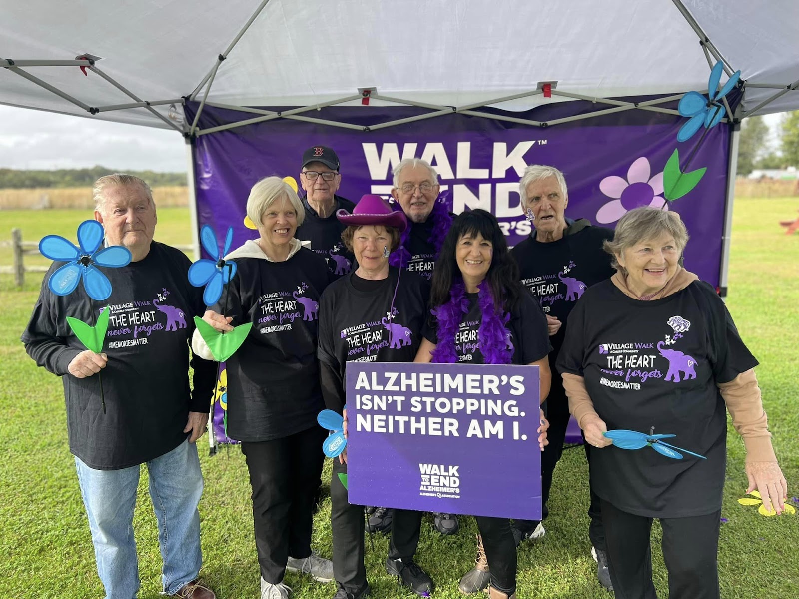 Village Walk elderly individuals standing in front of a sign advertising a Walk to End Alzheimer's event