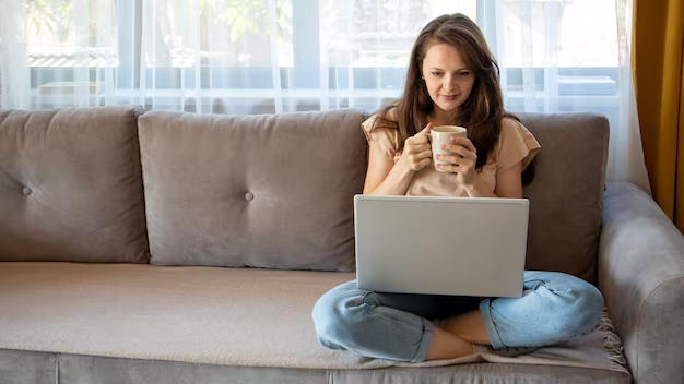 A girl looking at the laptop with a mug of coffee in her hand