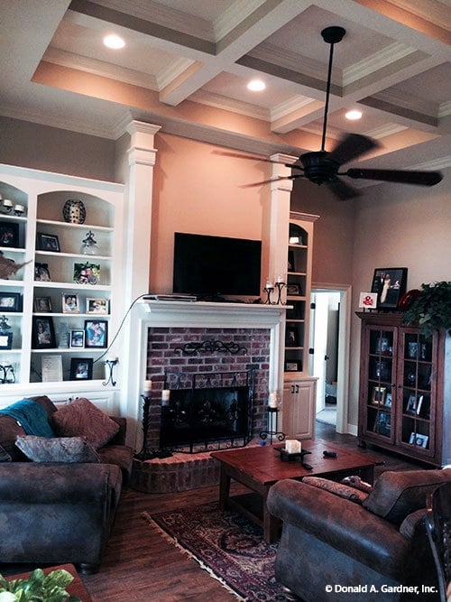 A brick fireplace, white built-ins, and an iron fan hanging from the coffered ceiling complete the living room.