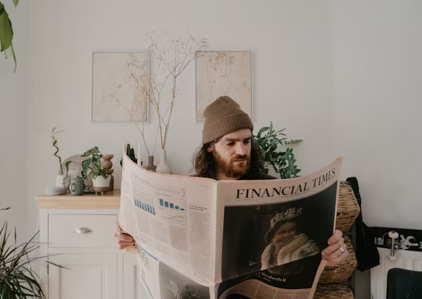 A man with a snow hat on and a beard reading the Financial Times news paper.
