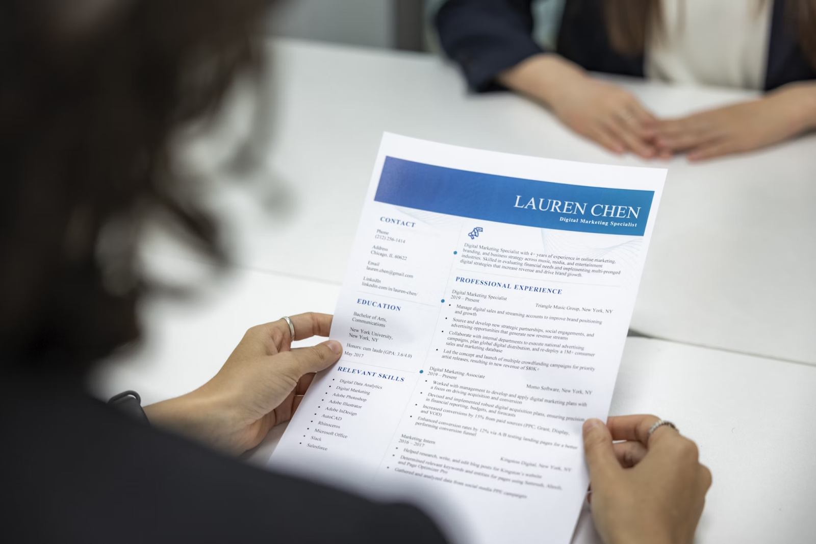 Female HR manager holding a CV and guiding on creating a powerful resume headline during a job interview, viewed from over her shoulder at the desk