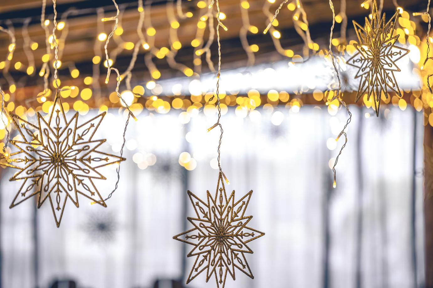 Golden star-shaped ornaments hanging from strings of warm fairy lights, creating a festive and cozy atmosphere with a blurred background of softly lit windows