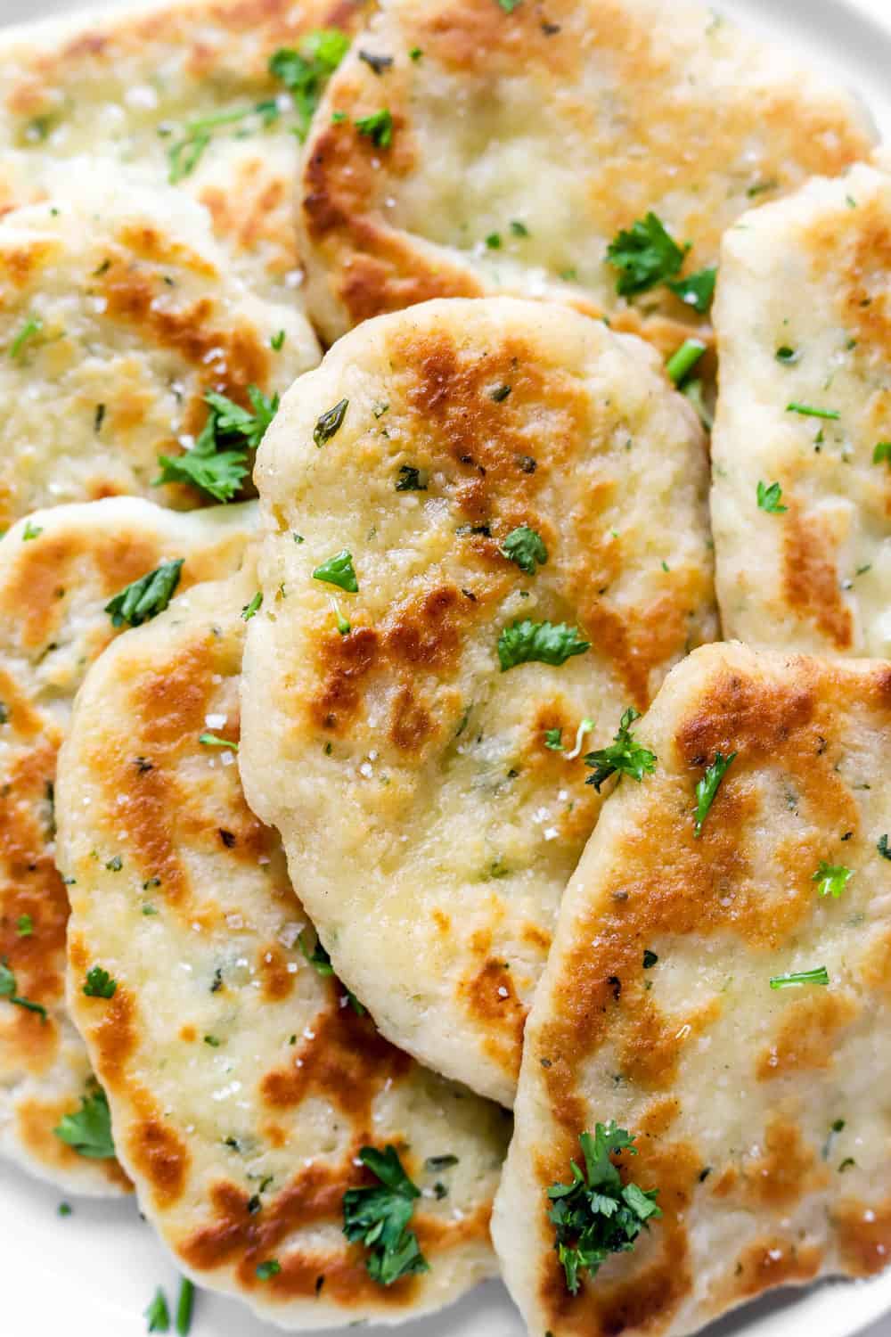 Close up of golden, fluffy gf naan bread with a garnish of sea salt and parsley.