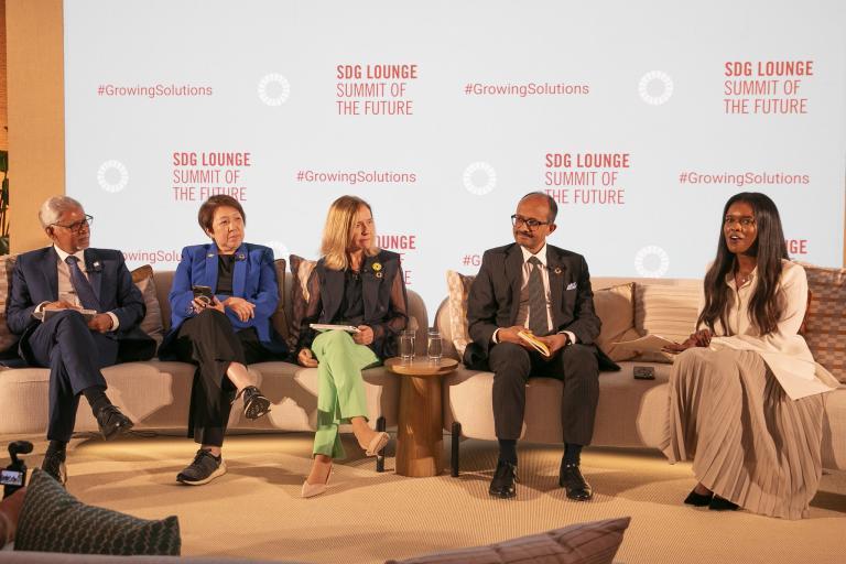 A group of five people seated on a stage engaging in a discussion during the SDG Lounge Summit of the Future. A backdrop behind them displays "SDG Lounge, Summit of the Future" and "#GrowingSolutions.