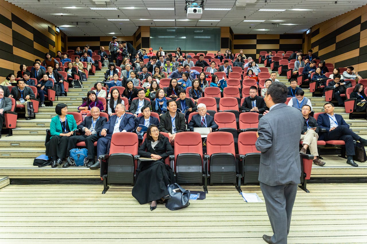 A diverse audience of professionals listening to a speaker in a lecture hall, demonstrating an educational setting that could be used for teaching elements of creating online courses.