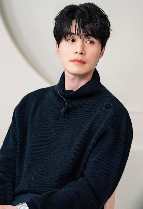 This contains an image of Lee Dong Wook with a black hair wearing a black sweater and white wrist watch, looking at the camera